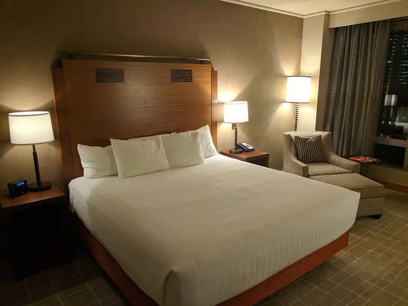 A made-up double bed with white bedding under warm bedside lamps